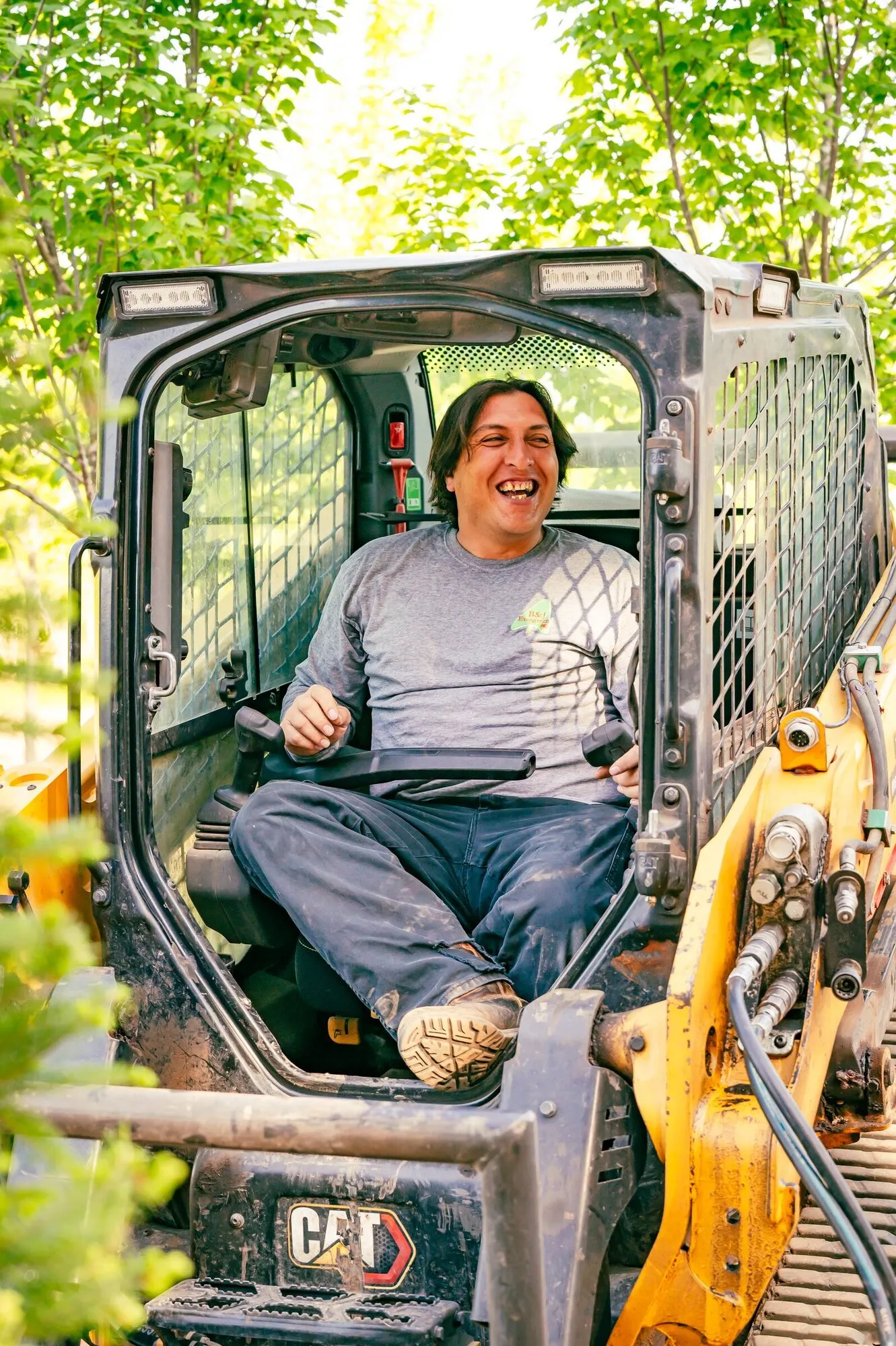Abraham smiling from the cab of a skid loader