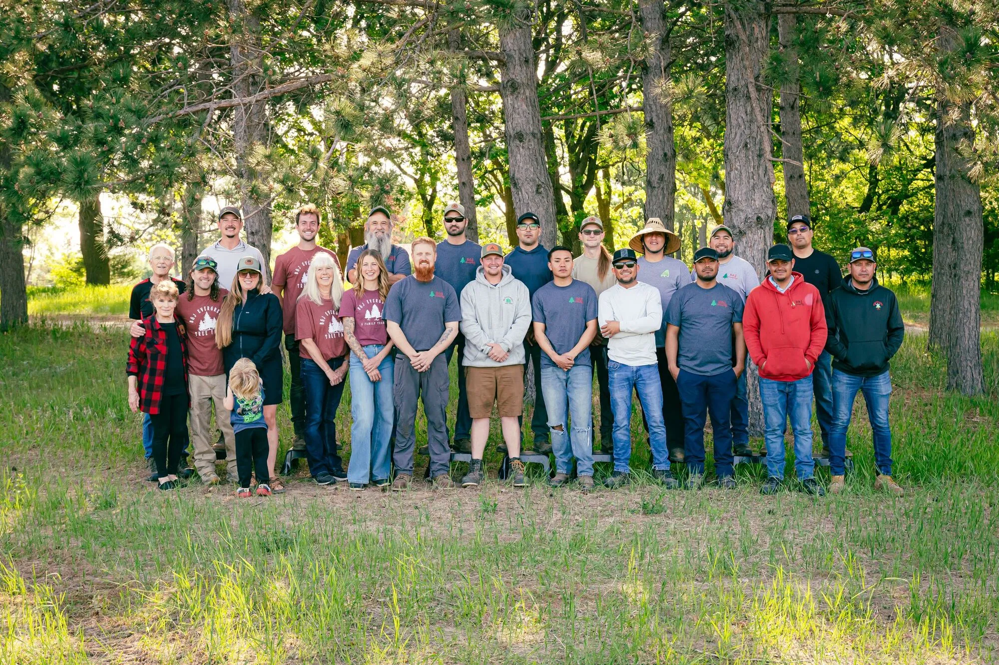 The full 2026 B&J Evergreen crew and the Johnson family lined up together under the pines on a sunny spring day