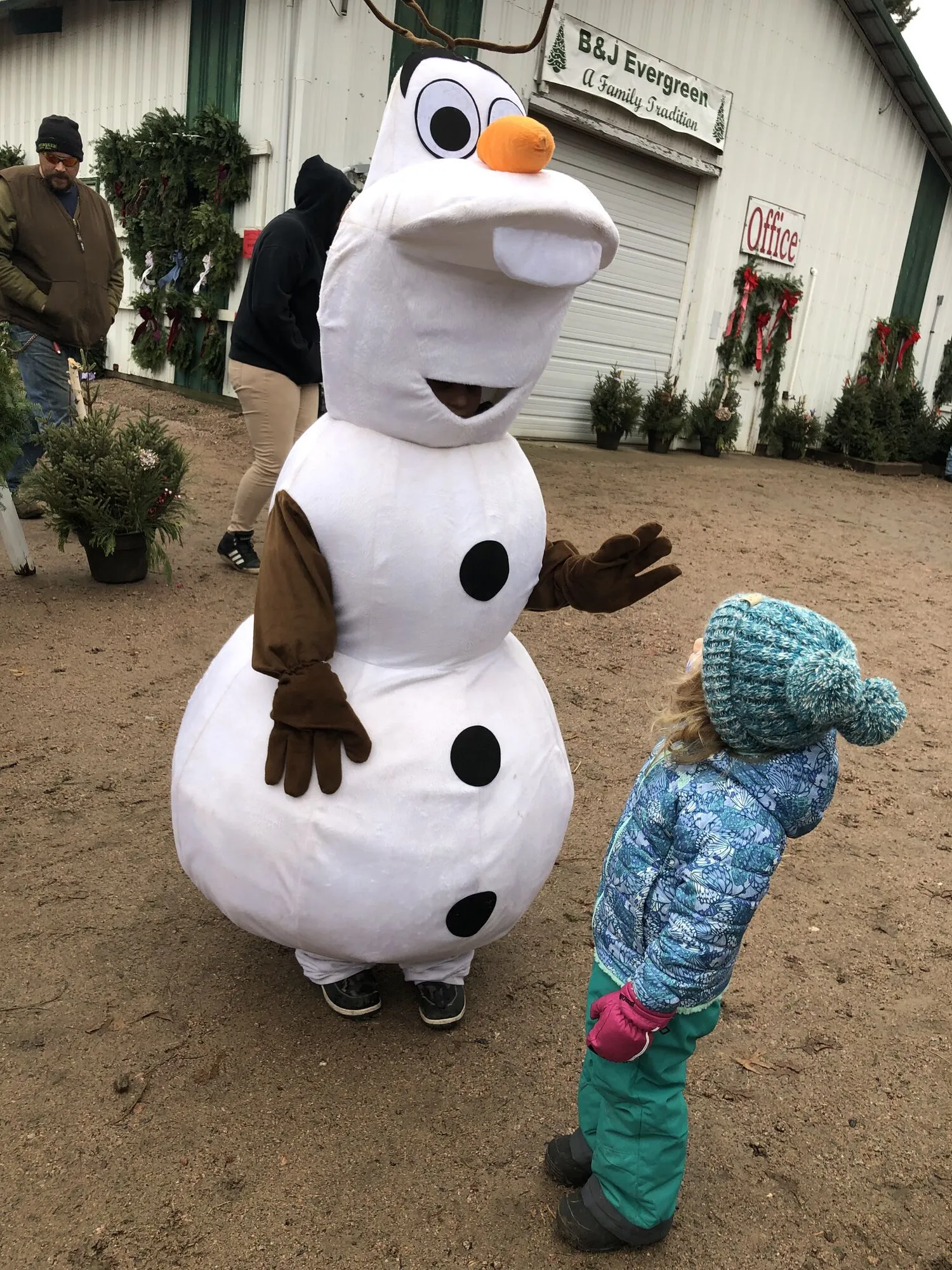 A young girl in a pink hat greeting a costumed snowman mascot outside the B&J Evergreen office