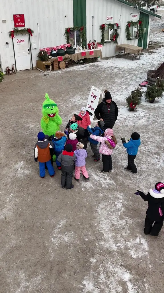 A person in a Grinch costume waving to a group of children outside the farm office