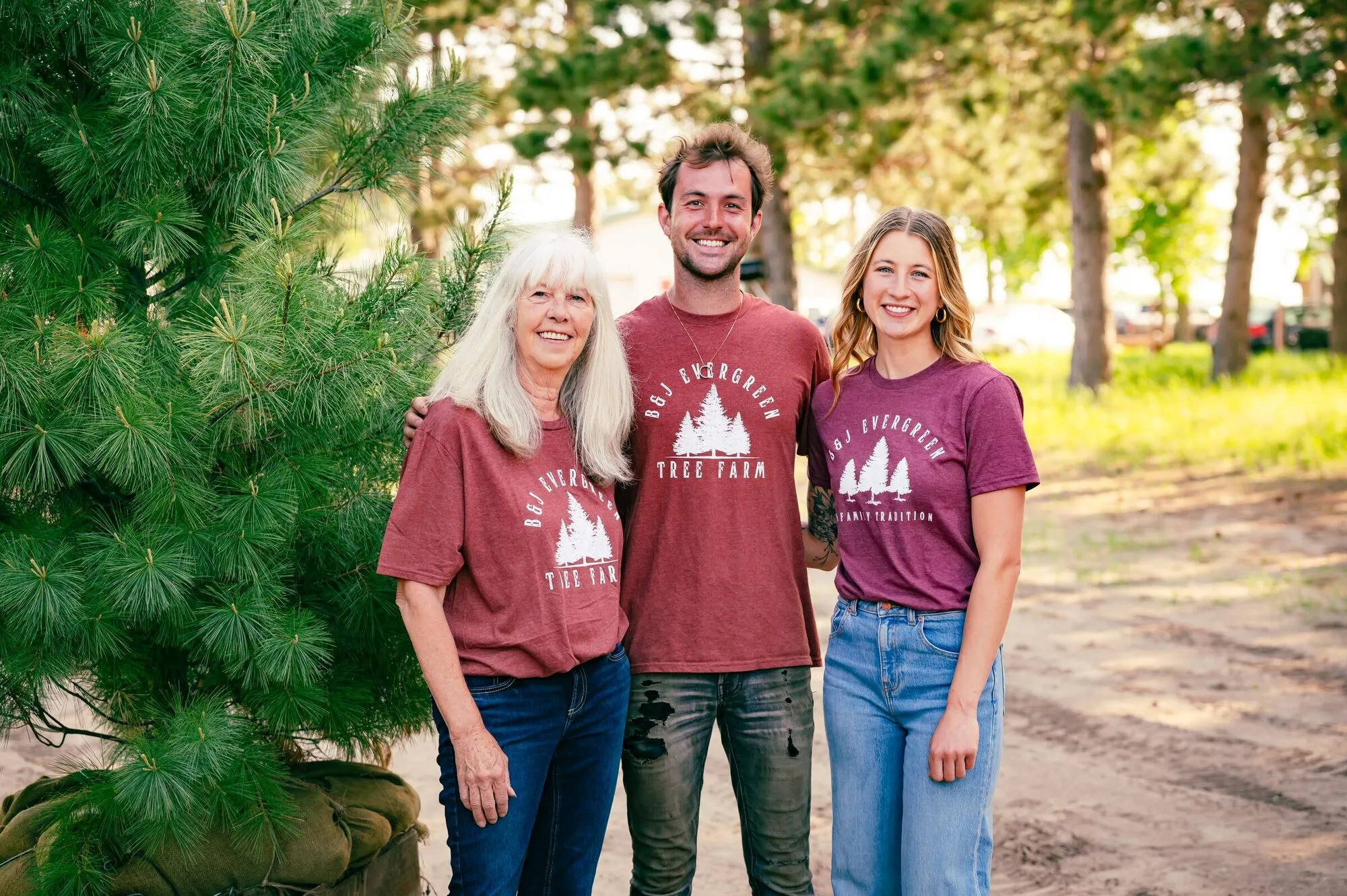 Brenda, Joey, and Kelly standing together in matching B&J Evergreen tees under the pines