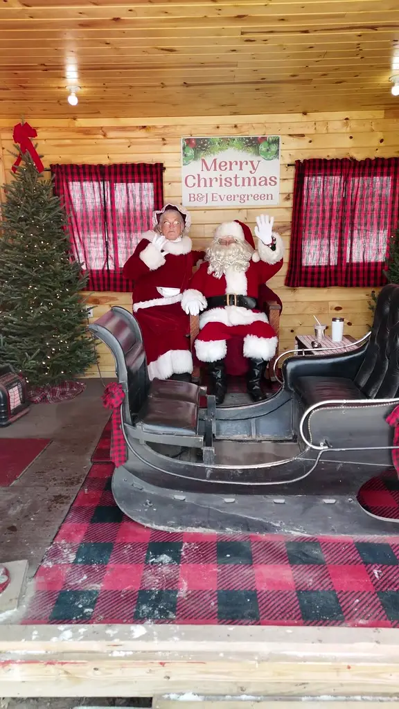 Santa and Mrs. Claus waving from an antique sleigh inside a decorated red cabin, pulling back to reveal the doorway
