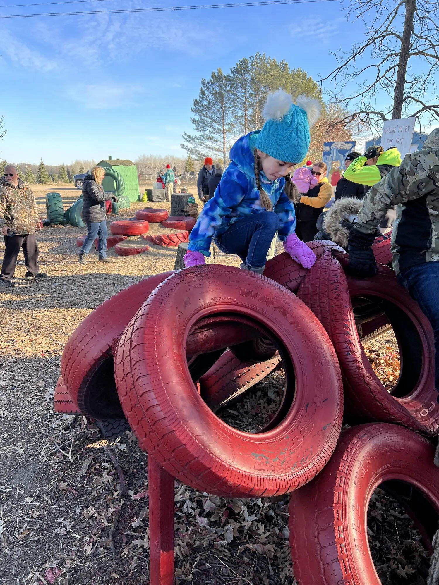 Kids climbing the red tire playground at the farm while their family shops for a tree nearby